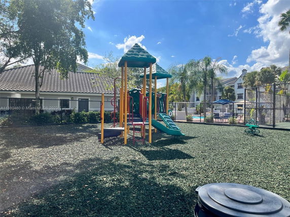 Outdoor playground with climbing structures and slides, surrounded by trees and a fence.