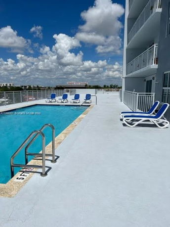 Rooftop with a swimming pool and lounge chairs next to a multi-story building.