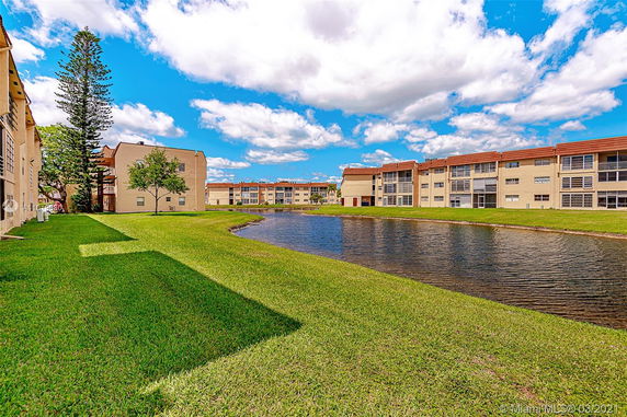 Buildings surrounding a pond with grass lawns.