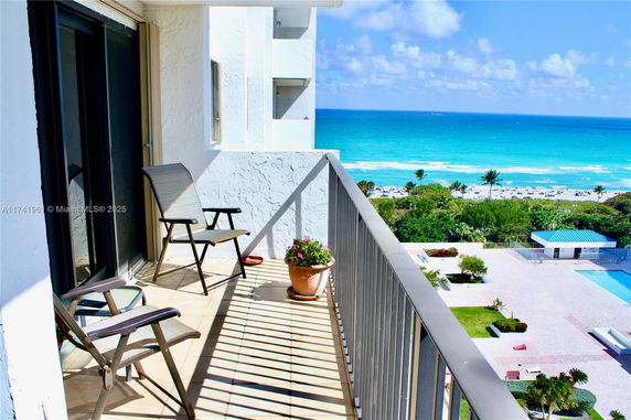 Balcony view of ocean and beach with chairs and railing.