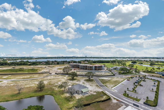 Panoramic view of a developing area with a building under construction, surrounded by open land, water bodies, and distant cityscape.