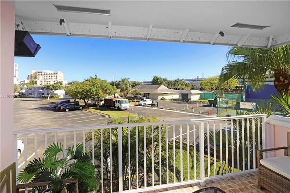 View from a balcony overlooking a parking lot and residential buildings.