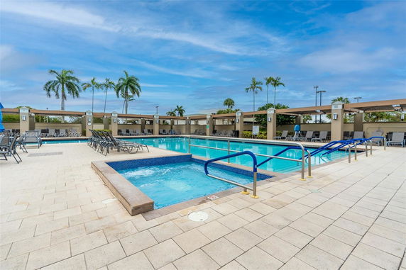 Outdoor swimming pool area with lounge chairs and palm trees.