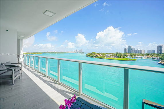 View from a modern balcony overlooking a turquoise water body and a distant cityscape.