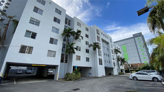 Front view of a multi-story apartment building with parking space beneath.