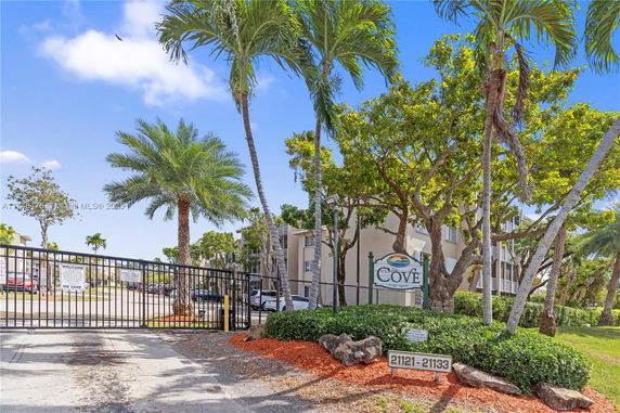 Front view of a gated residential complex with trees and a sign reading 'The Cove'.