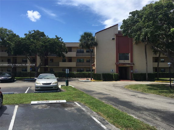 Exterior view of a multi-story apartment building with a parking area in front.