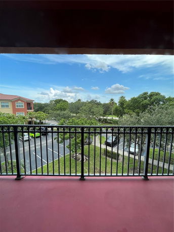 View from a balcony overlooking a parking lot and surrounding greenery.