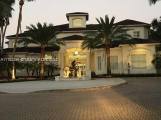 Front view of a large multi-story house with a grand entrance and palm trees.