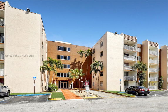 Front view of a multi-story apartment building with balconies and palm trees.