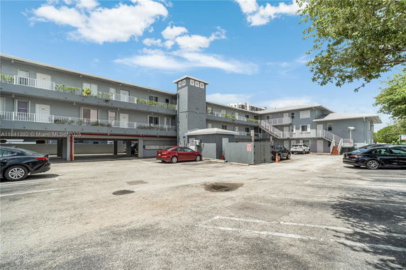 Front view of a multi-story residential building with exterior corridors and parking area.