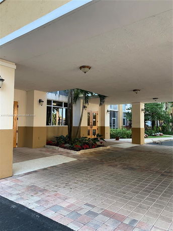 Front view of a building entrance with covered walkway and decorative plants.