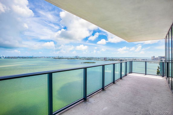 Balcony with glass railing overlooking a panoramic view of water and cityscape.