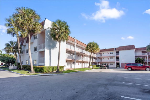 Front view of a multi-story apartment building with balconies and a parking area.