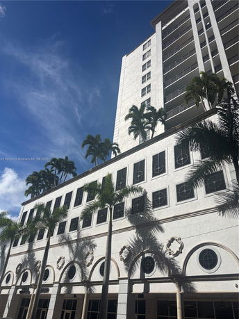 Front view of a multi-story building with tall palm trees and distinctive circular windows.