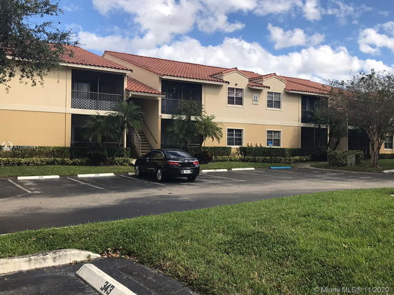 Parking area in front of a two-story building with a red tile roof.