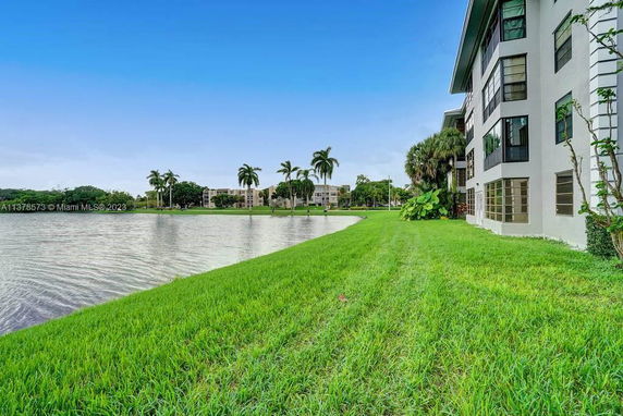 View of a lake and grassy area with a multi-story building in the background.