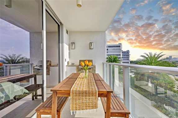 View from a balcony with a table and chairs overlooking a cityscape and trees.