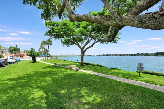 View of a lakeside area with trees, benches, and a pathway.