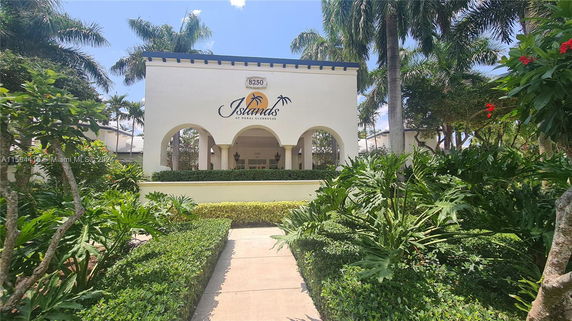 Front view of a clubhouse building with arches and palm trees in the foreground.