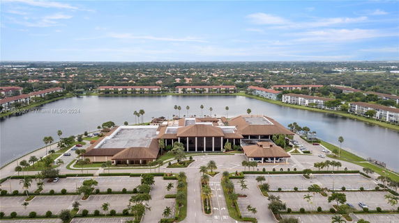 Aerial view of a large building complex with a parking lot and a lake surrounded by residential buildings.