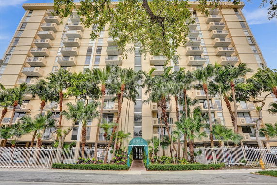 Front view of a tall residential building with multiple balconies and palm trees.