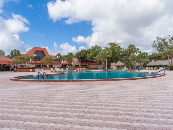 Outdoor area featuring a large swimming pool with a surrounding patio and nearby buildings.