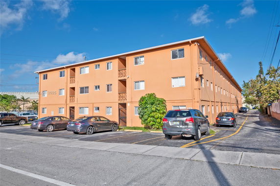 Front view of a three-story apartment building with multiple parking spaces.