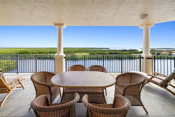 Outdoor balcony with wicker furniture overlooking a body of water and greenery.