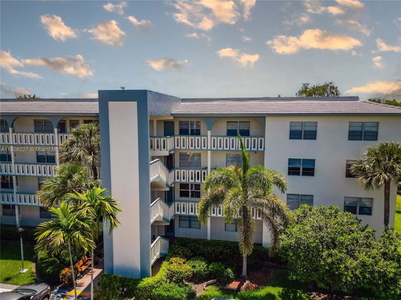 Front view of a multi-story residential building with balconies and palm trees in front.