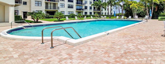 Front view of a multi-story residential building with balconies, adjacent to a swimming pool.