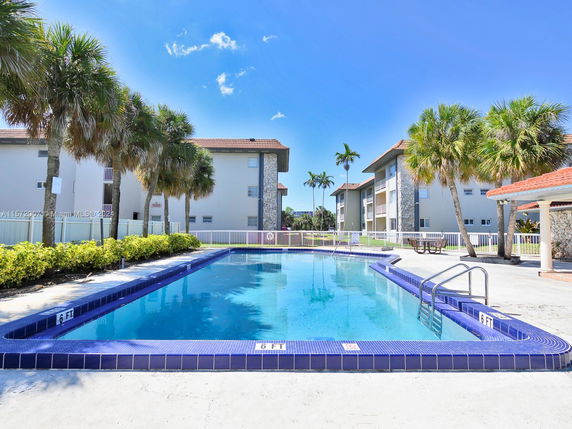 Outdoor swimming pool surrounded by residential buildings and palm trees.
