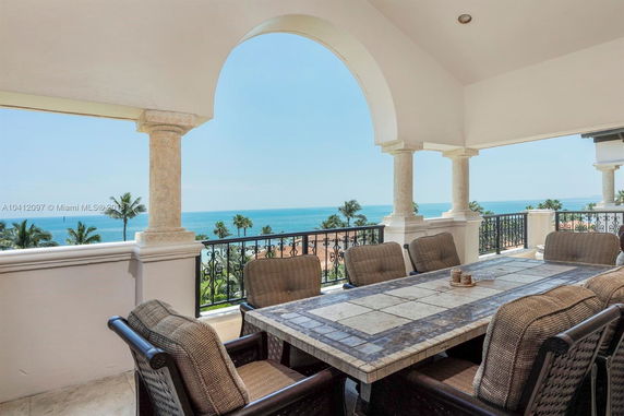 Outdoor seating area with a view of the ocean and palm trees.