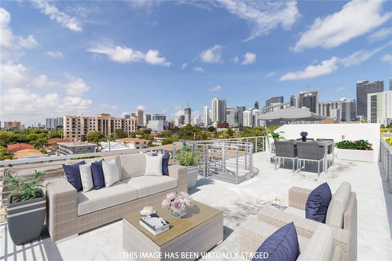 Rooftop view with outdoor seating area, table, chairs, and city skyline in the background.