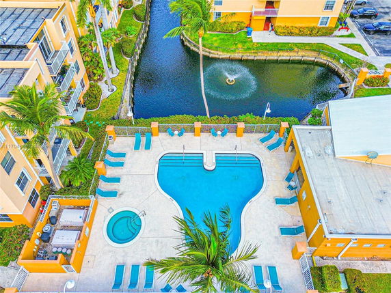 Aerial view of a swimming pool area with lounge chairs, surrounded by buildings and a canal.