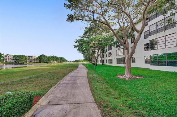 Side view of a multi-story building next to a walkway and greenery.