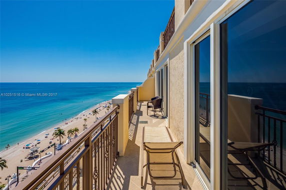 Coastal view from a high-rise building with balconies and glass windows overlooking a sandy beach and ocean.