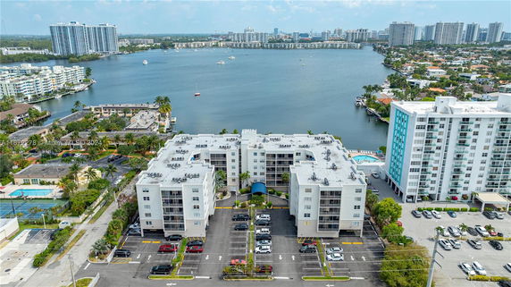 Aerial view of residential buildings with rooftops featuring air conditioning units and parking area in front, near a water body.