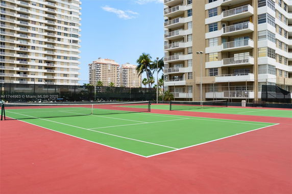 Tennis court outside multi-story apartment buildings.