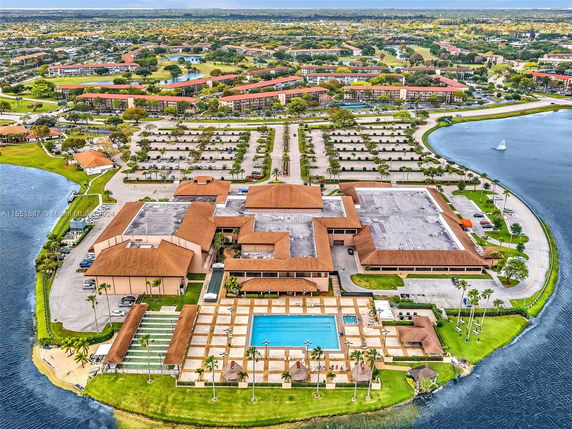 Aerial view of a large building complex featuring a swimming pool, surrounded by parking and water bodies.