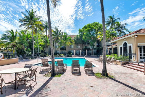 Outdoor area with a swimming pool surrounded by palm trees and multi-story buildings.