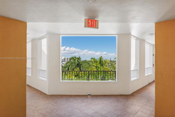 View of surrounding area with palm trees and buildings seen from a balcony with tiled floor and exit sign.