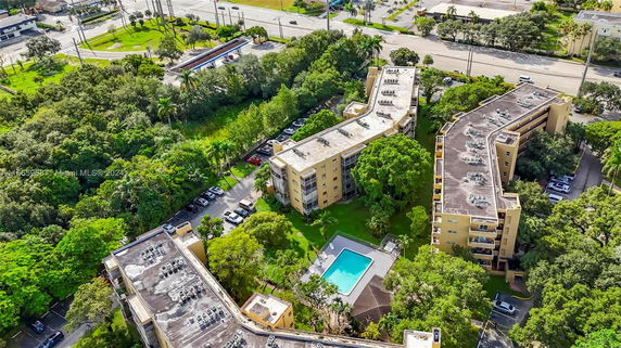 Aerial view of residential buildings with a swimming pool surrounded by trees and parking areas.