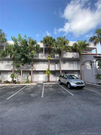 Outdoor parking area in front of a multi-story building with balconies and palm trees.