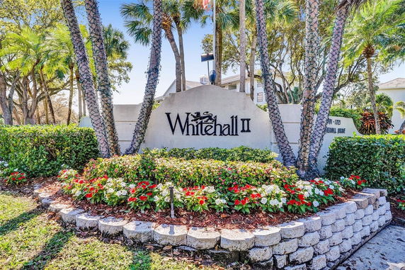 Entrance sign for Whitehall II surrounded by flowers and palm trees.