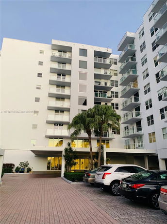 Front view of a multi-story apartment building with balconies and a parking area.