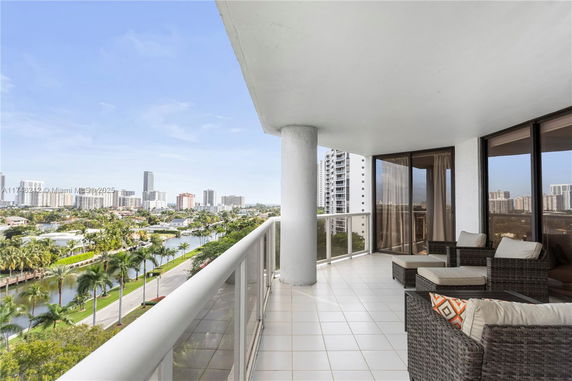 Balcony with outdoor furniture offering a view of city skyline and waterway.