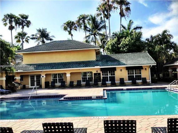 Outdoor swimming pool area in front of a two-story building with a tiled roof.