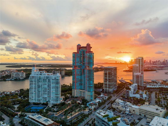 Panoramic view of a cityscape featuring multiple high-rise buildings and a body of water during sunset.
