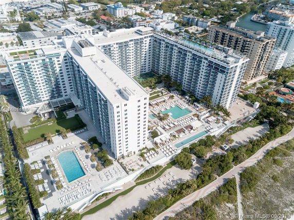 Aerial view of a large multi-story building complex with multiple swimming pools and surrounding urban area.